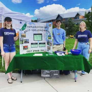 students in Geography club t-shirts at a table event outdoors 